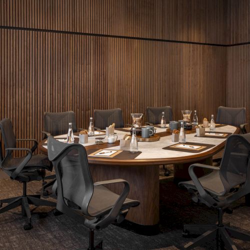 A modern conference room with a long table, wheeled office chairs, and coffee/tea service items set for a meeting.