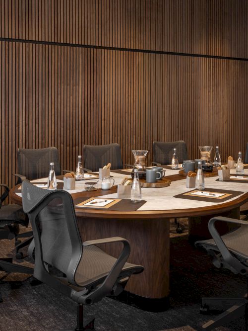 A modern conference room with a long table, wheeled office chairs, and coffee/tea service items set for a meeting.