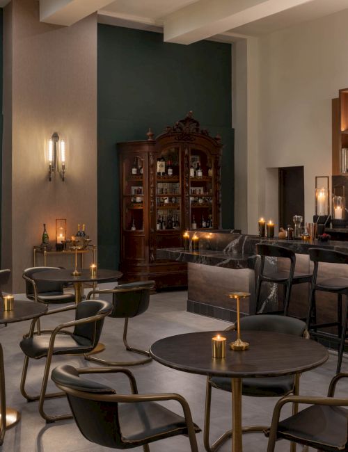 A luxury lounge bar with marble counter, stocked bottles, candlelit seating, and an elegant glass cabinet in warm lighting.