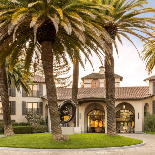A sunny campus scene with palm trees and a classic building, creating a warm, inviting atmosphere.