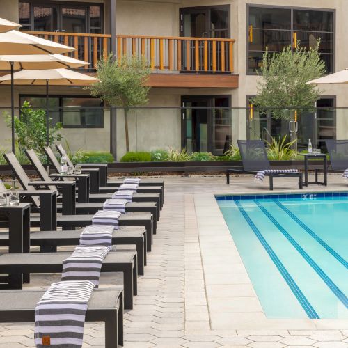 A poolside hotel with sun loungers and umbrellas, a calm courtyard, and a two-story building in the background. End.