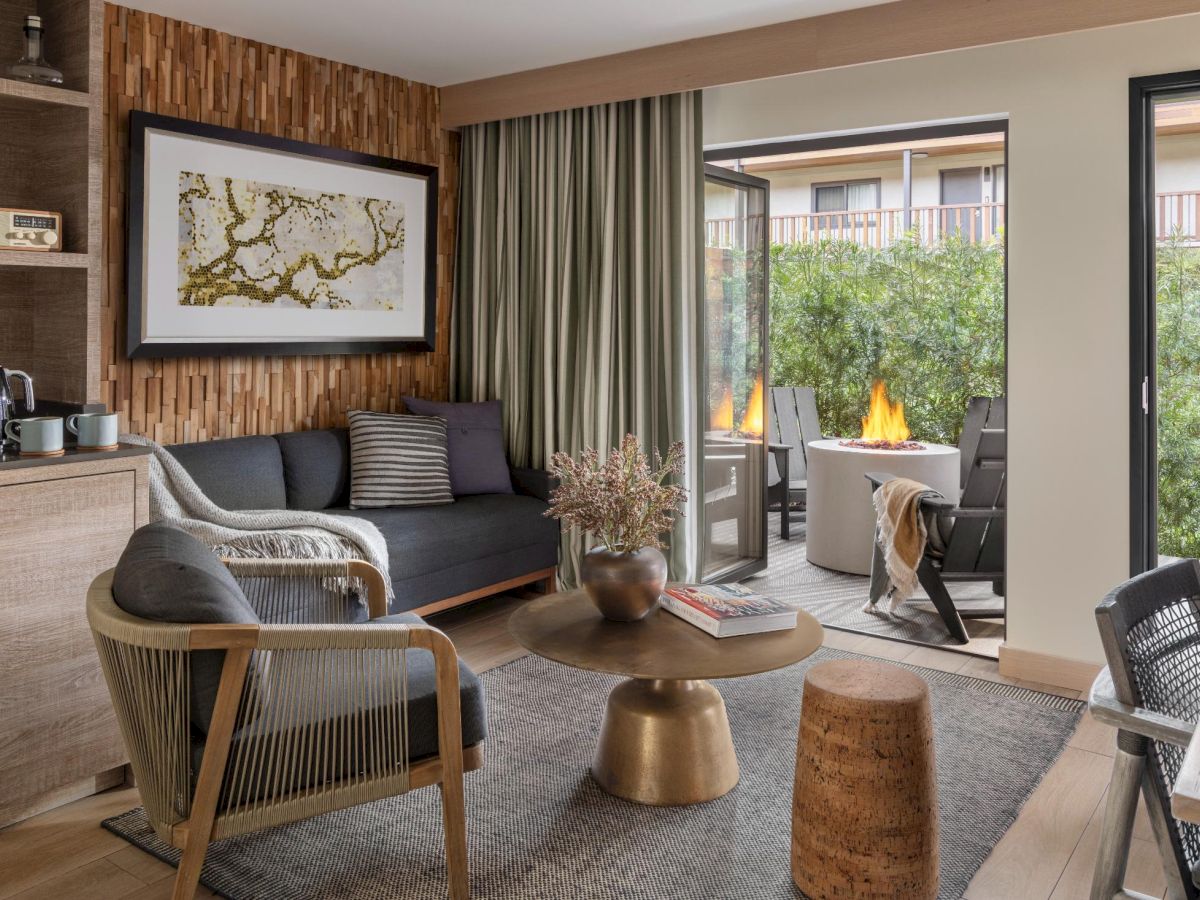 A modern living room with a wood-paneled feature wall, gray sofa, armchairs, coffee table, map art, and a sliding door to a patio with a fire pit outside.