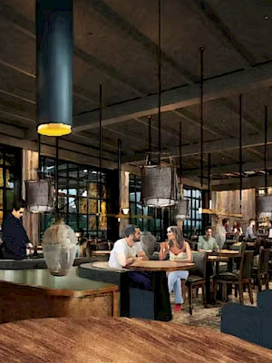 A modern, busy restaurant with wooden floors, blue pendant lights, and patrons seated at tables; a server attends in the background.