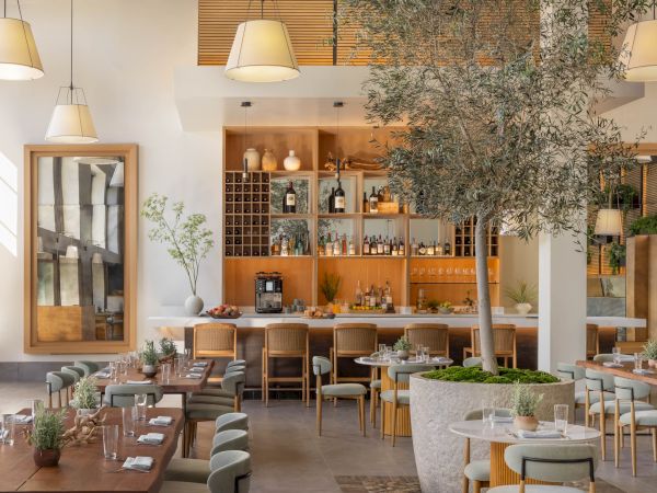 A stylish restaurant interior with pendant lamps, a wine bar stocked with bottles, bamboo decor, and neatly set dining tables.