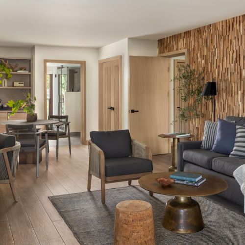 A cozy living room with a brick accent wall, comfy seating, a coffee table, TV, and a dining area in the background, modern and inviting.