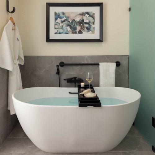 A modern spa-like bathroom: freestanding white tub, candle and glass, towel on rail, and framed art on the wall.
