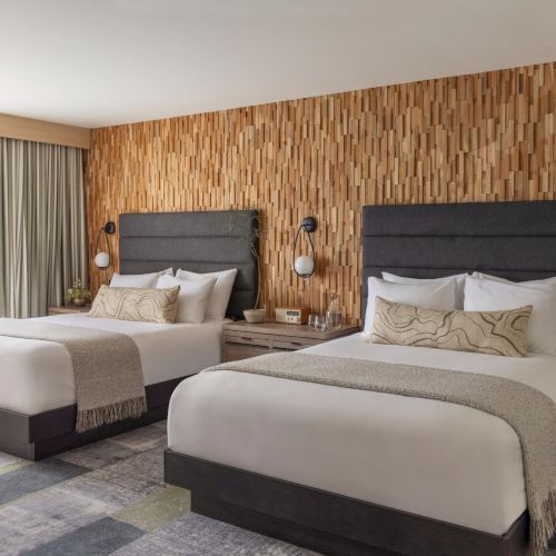 A cozy hotel bedroom with two double beds, wood-paneled walls, a glass door to a balcony, and soft natural light ending the sentence.