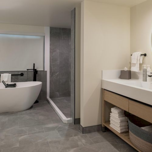 A small bathroom with a beige color scheme: sink with mirror, a towel rack, and a sunlit window; appears tidy and compact.