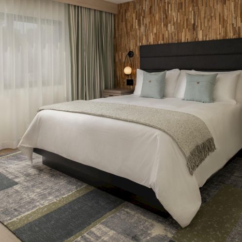 A modern hotel bedroom with a large bed, plush bedding, nightstands, and a warm, wood-paneled accent wall, cozy and inviting.