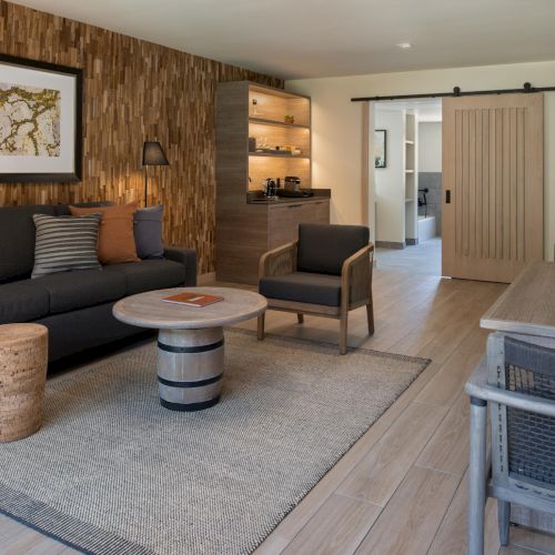 A cozy living room with a gray sectional, round coffee table, warm lighting, a fireplace, and a flat-screen TV; modern, welcoming space.