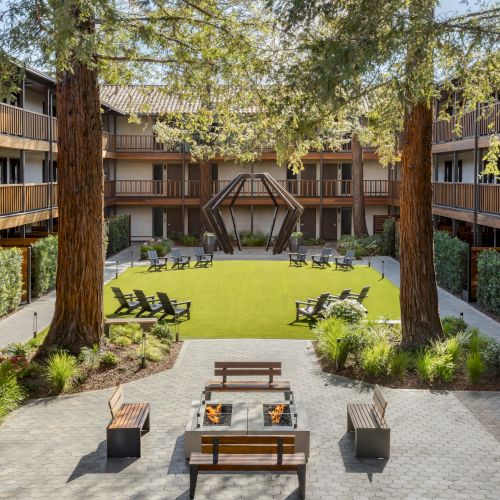 A tranquil courtyard inside a hotel or apartment complex, with a central lawn, trees, and seating around a paved area; hotel-style atrium feel.