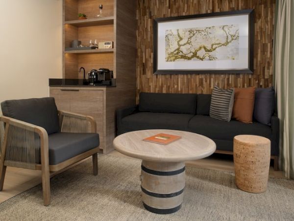 A modern hotel-style living area with a dark sofa, wooden armchair, round marble coffee table, and a textured wood feature wall, ending the sentence.