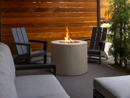 A modern outdoor seating area with a circular fire pit, gray couches, and wooden privacy wall.