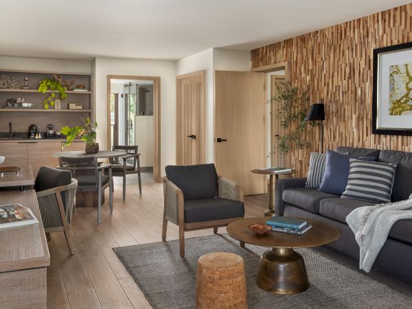 A bright modern living room with a sofa, coffee table, and an open kitchen featuring wood paneling and plants.