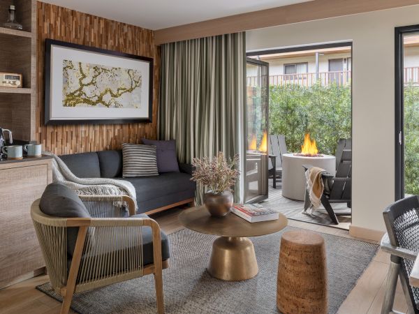 Modern lounge with a sofa, framed art, and an outdoor fire pit patio visible through wide doors, warmly inviting.