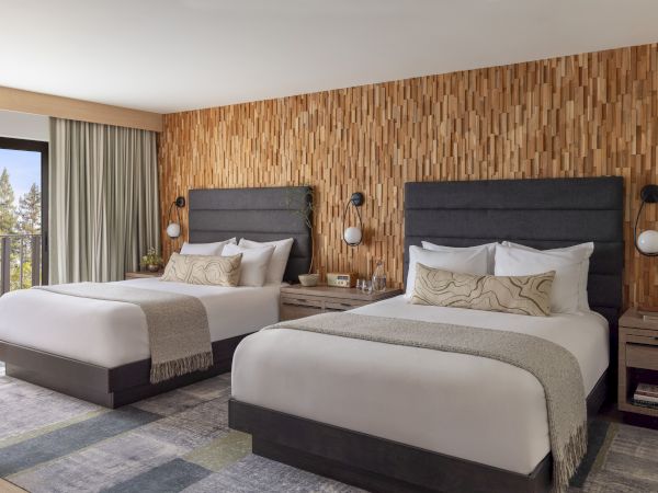 Modern twin bedroom with two beds, gray headboards, glowing bedside lamps, and a carved wood wall accent.