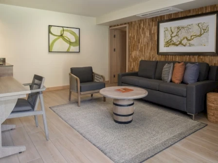 A modern living room with a gray sofa, matching armchairs, a round coffee table, a light rug, and abstract art on the walls.