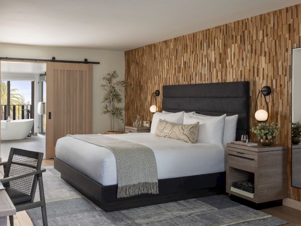 Modern bedroom with a large bed, wooden 3D wall, twin globe lamps, and open doors to a bathroom and balcony.