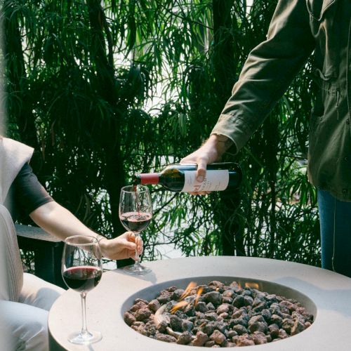 Two people enjoying a small outdoor setup by a fire pit, and a person pouring wine into a glass.