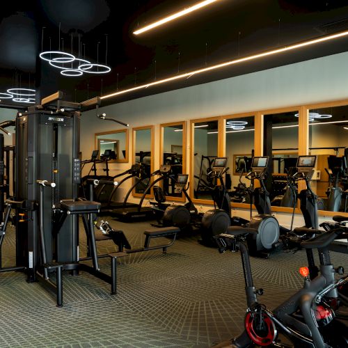 A modern gym interior with cardio and strength machines, mirrors, and warm lighting; fitness equipment scattered around a spacious workout area.