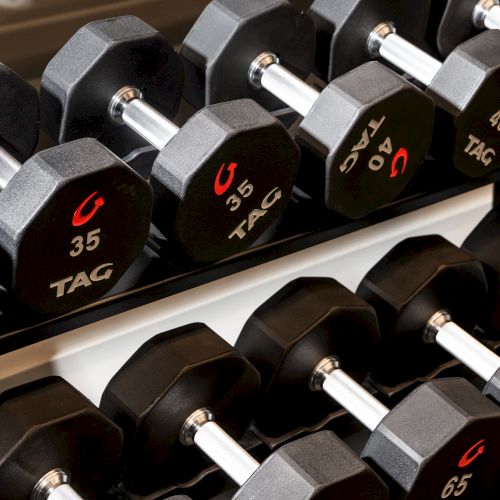 A row of black hex dumbbells on a rack, labeled with weights like 30, 35, and 40 in red and white, with chrome handles.