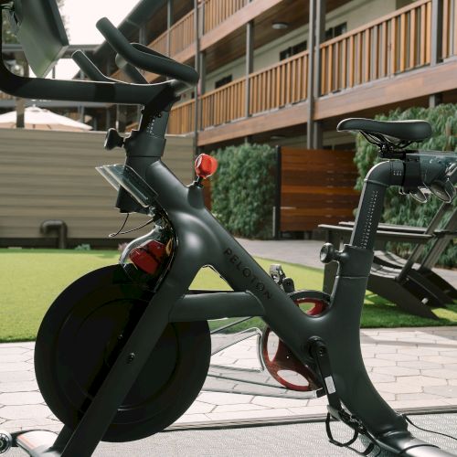 A matte black cargo-style bicycle with a front hub motor and a rear hub, urban setting, two-tier building in the background, close-up shot.