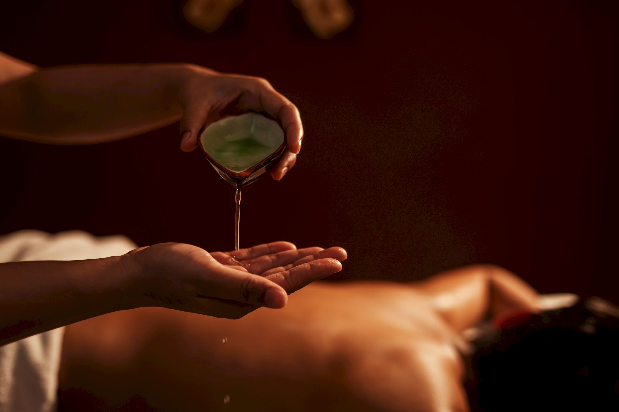 Someone pours oil or liquid onto another person&rsquo;s body in a spa or massage setting, suggesting a ritual or treatment.
