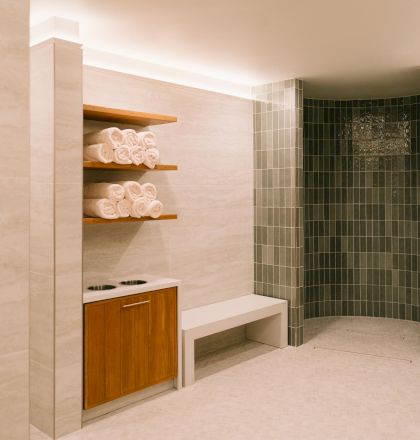 A small, modern bathroom with a wooden shelf and open cabinet, tiled floor, and a shower area with glass door in the back.