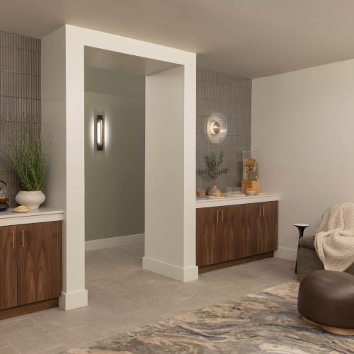 Modern lounge/spa interior with built-in cabinetry, wall art light fixtures, a cozy sofa, and a tea/refreshment counter by a textured wall.