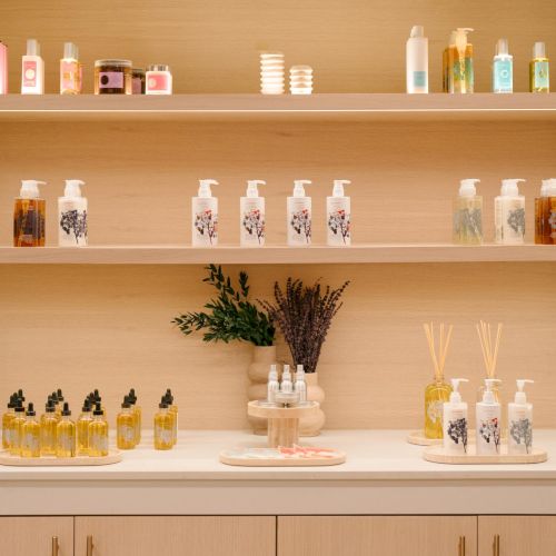 A tidy shelf display with small bottles, jars, and a vase of flowers on light wooden shelves.