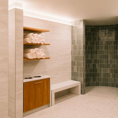 An entryway to the spa with open shelves and towels, and a tiled shower area to the right, all in neutral tones.
