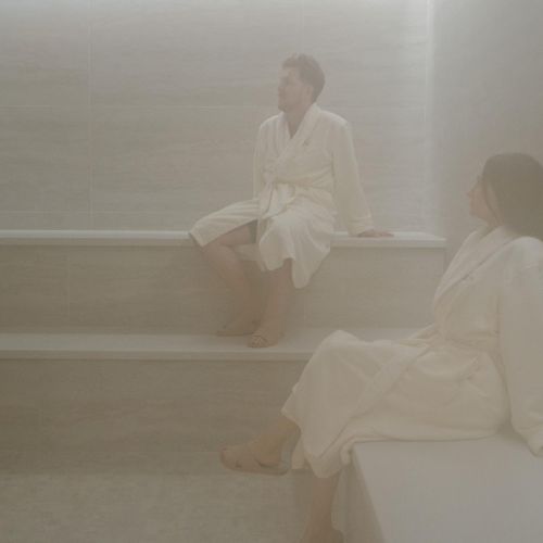 Two people in robes, sitting and enjoying a steam room.