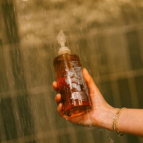 A hand holds a small bottle of body wash.