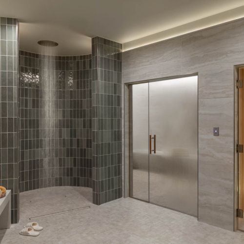 A modern spa-like bathroom with a tiled steam shower, glass doors, rain shower head, and warm wood sauna room.