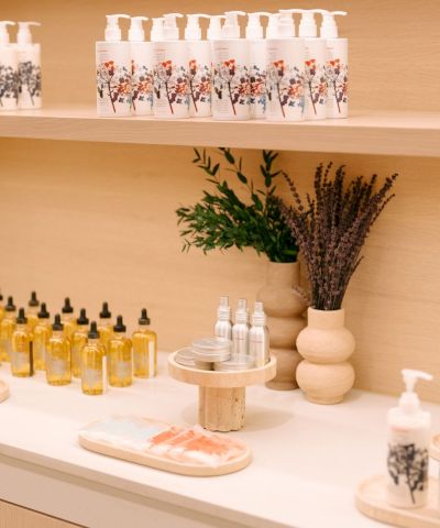 A bright, minimalist spa display with lotion bottles, essential oils, and reed diffusers on a white counter and shelves.