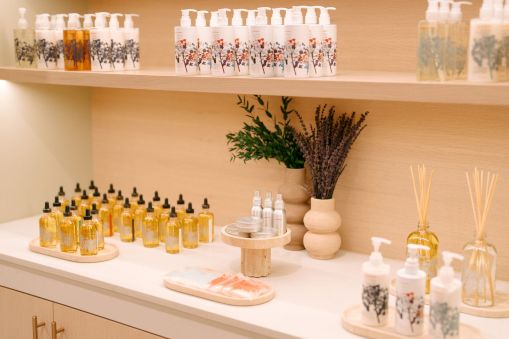 A bright, minimalist spa display with lotion bottles, essential oils, and reed diffusers on a white counter and shelves.