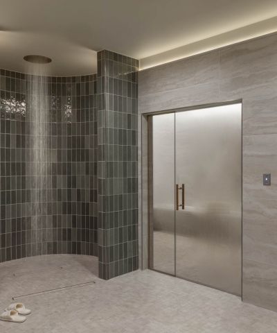 A modern tiled spa bathroom with a glass walk-in steam shower, LED lighting, and a wooden sauna area with doors.