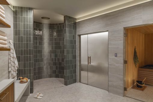 A modern tiled spa bathroom with a glass walk-in steam shower, LED lighting, and a wooden sauna area with doors.