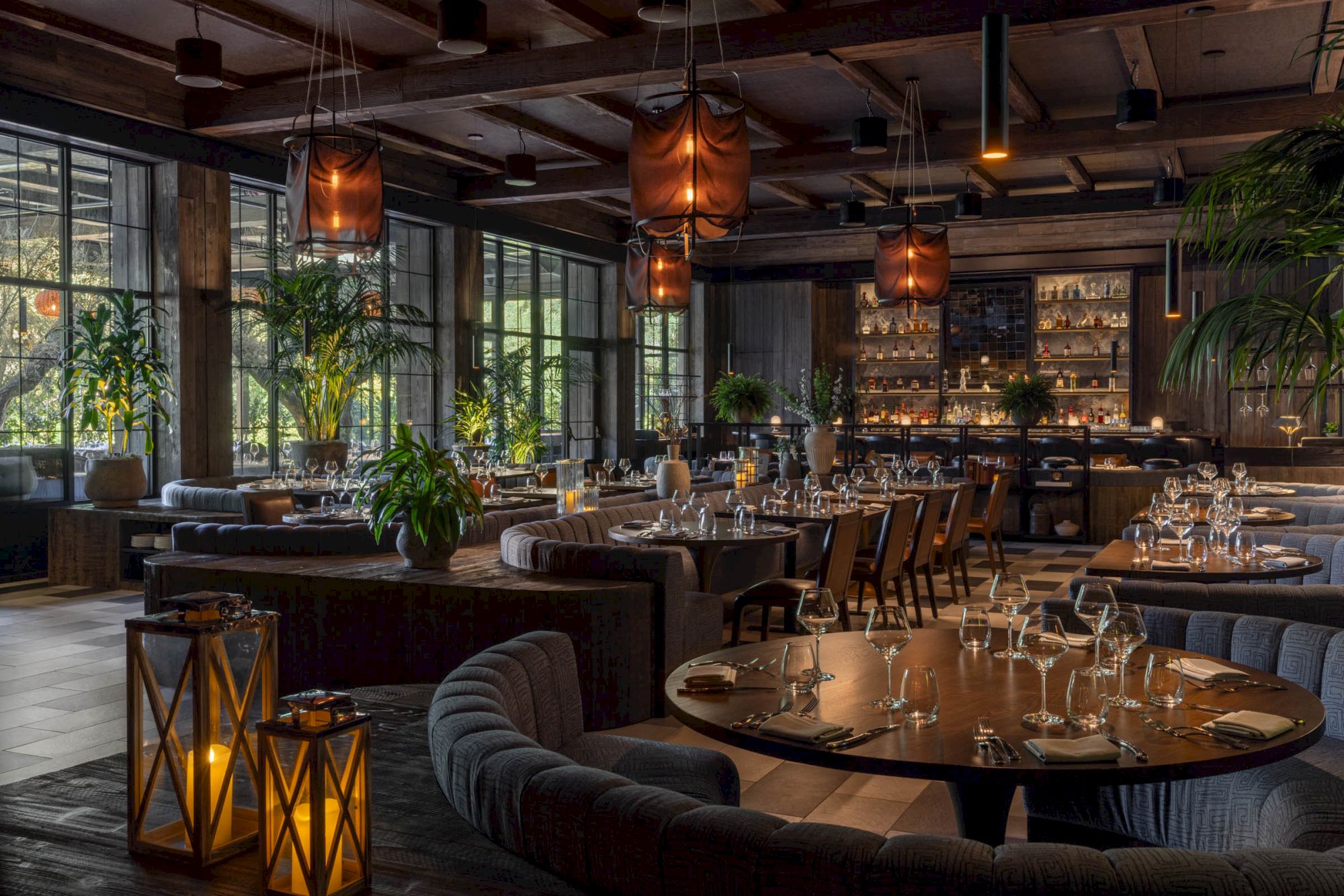 A cozy restaurant/bar with set tables, plants, warm lantern lighting, and boxing heavy bags hanging from the ceiling.
