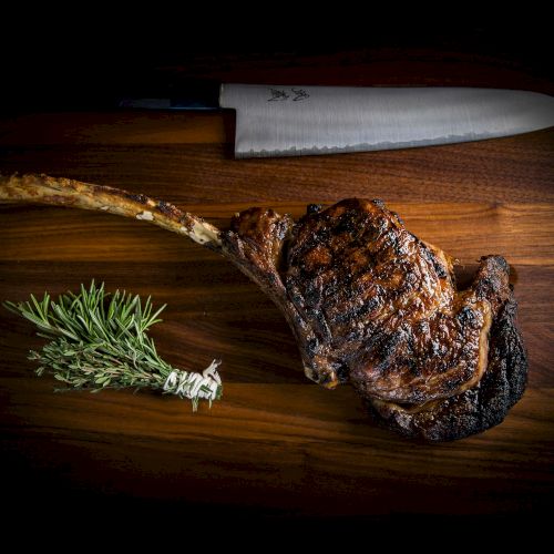 A single roasted leg of lamb with a charred crust sits on a wooden board, a chef&rsquo;s knife above, and a sprig of rosemary beside it, all lit dramatically.