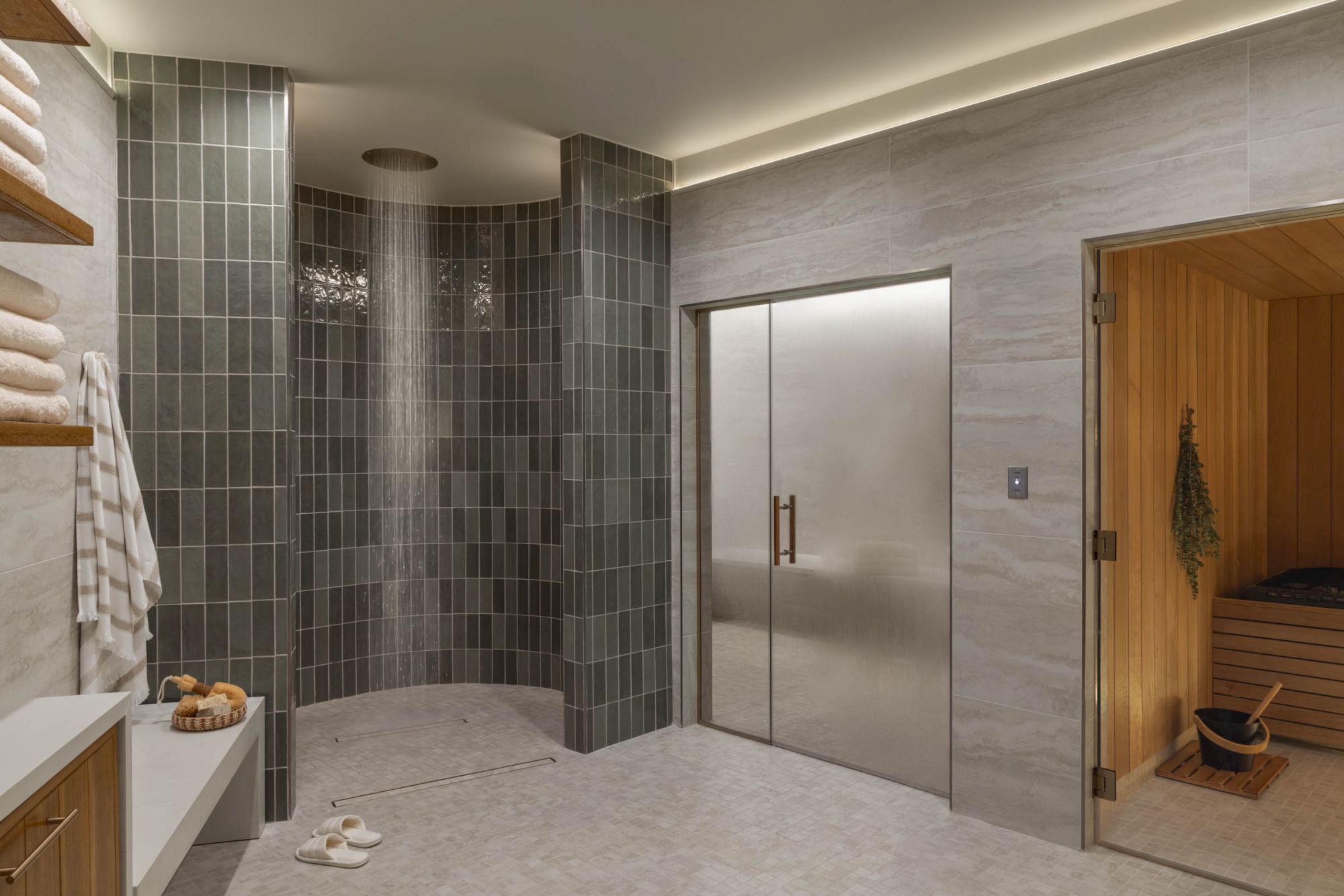A modern spa bathroom with a tiled walk-in shower, rainfall showerhead, steam-like enclosure, and warm wood sauna door.
