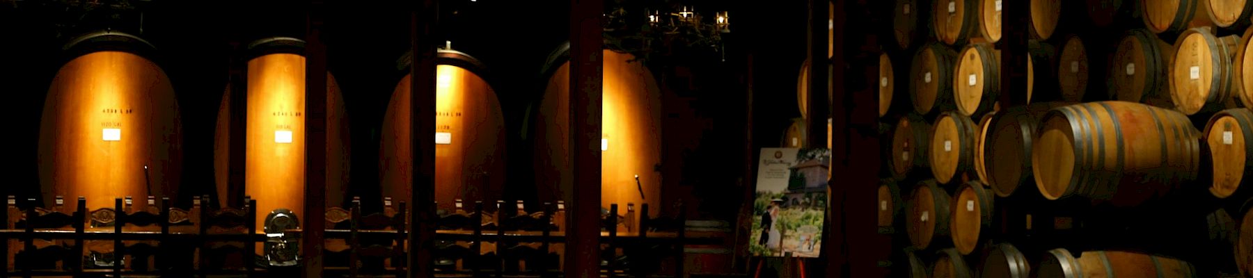 A dim winery cellar with rows of oak barrels and casks under warm lantern light.