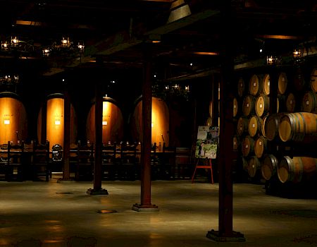 A dim winery cellar with rows of oak barrels and casks under warm lantern light.